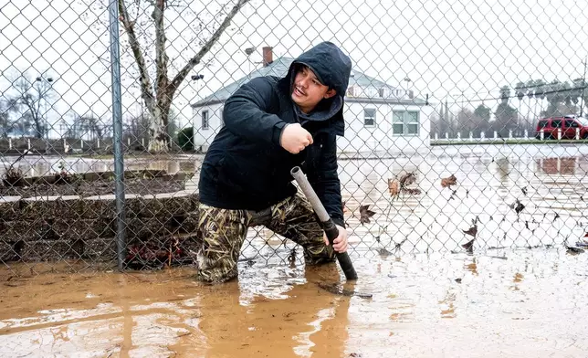 Dekoda Cruz works to clear a drain following heavy rains on Monday, Dec. 22, 2025, in Redding, Calif. (AP Photo/Noah Berger)