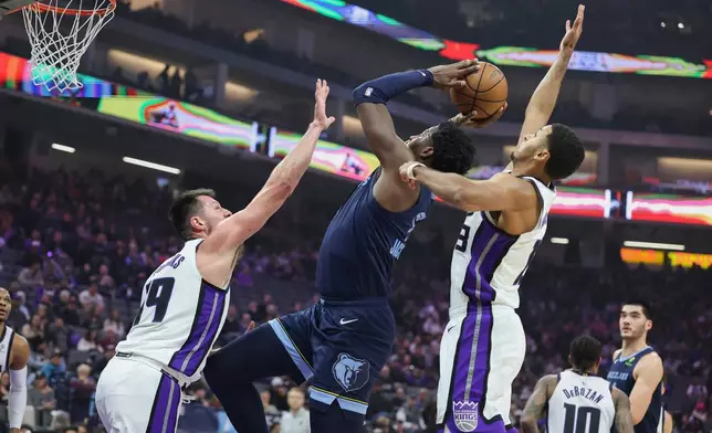 Memphis Grizzlies forward Jaren Jackson Jr., center, attempts to go up for a shot with Sacramento Kings center Drew Eubanks, left, and forward Keegan Murray, right, defending during the first half of an NBA basketball game Sunday, Nov. 30, 2025, in Sacramento, Calif. (AP Photo/Sara Nevis)