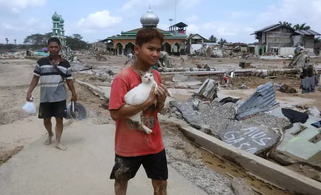 A survivor holds a cat as he walks at an area devastated by flash flood in Aceh Tamiang on Sumatra Island, Indonesia, Friday, Dec. 5, 2025. (AP Photo/Binsar Bakkara)