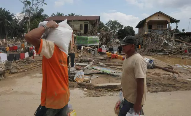 Survivors carry relief goods at an area devastated by flash flooding in Aceh Tamiang on Sumatra Island, Indonesia, Friday, Dec. 5, 2025. (AP Photo/Binsar Bakkara)