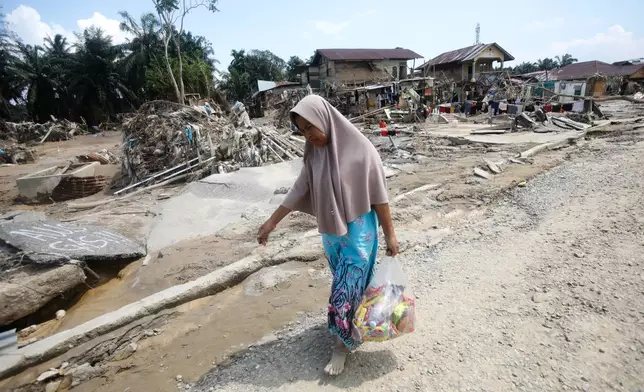 A survivor carries relief goods at an area devastated by flash flooding in Aceh Tamiang on Sumatra Island, Indonesia, Friday, Dec. 5, 2025. (AP Photo/Binsar Bakkara)