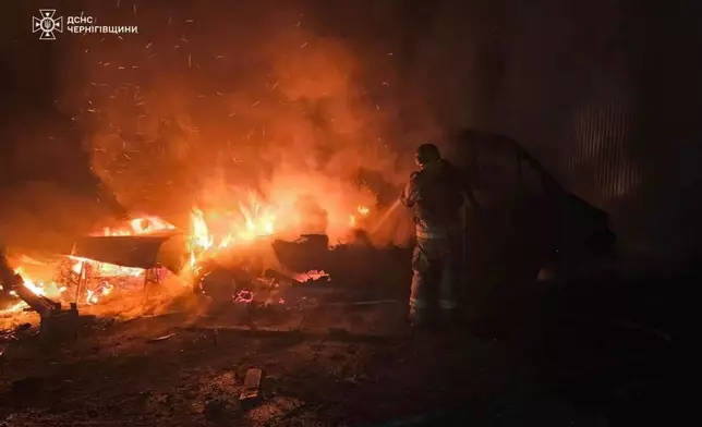 In this photo provided by the Ukrainian Emergency Service on Tuesday, Dec. 23, 2025, a rescue worker puts out a fire of a car destroyed a Russian strike in Chernihiv region, Ukraine. (Ukrainian Emergency Service via AP)