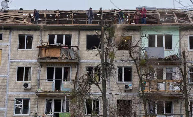Municipal workers clean debris on the roof after a Russian drone hit an apartment building during an aerial attack in Kyiv, Ukraine, Tuesday, Dec. 23, 2025. (AP Photo/Efrem Lukatsky)