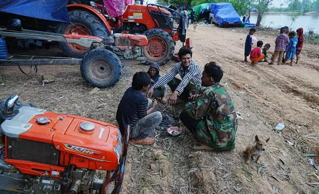 People warm themselves near a flame as they take refuge in Srey Snam, Siem Reap province, Cambodia Wednesday, Dec. 10, 2025, after fleeing from home following a fighting between Thailand and Cambodia over territorial claims. (AP Photo/Heng Sinith)