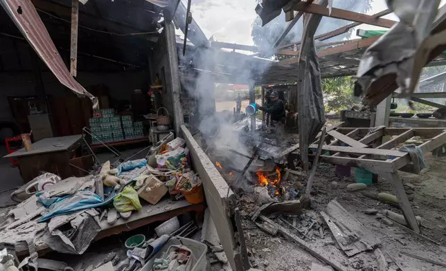 A Thai police officer splashes water to control fire at a house which, Thai local security forces say, was damaged by a Cambodian artillery in Surin province, Thailand, Thursday, Dec. 11, 2025. (AP Photo/Wason Wanichakorn)