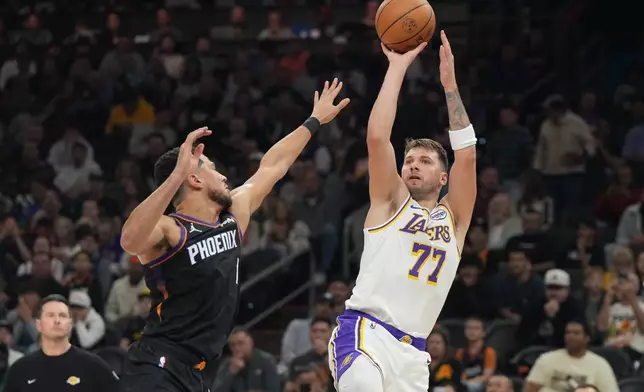 Los Angeles Lakers guard Luka Doncic (77)looks to shoot over Phoenix Suns guard Devin Booker, front left, during the first half of an NBA basketball game, Sunday, Dec. 14, 2025, in Phoenix. (AP Photo/Rick Scuteri)