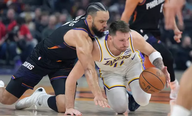 Phoenix Suns forward Dillon Brooks, left, and Los Angeles Lakers guard Luka Doncic, right, battle for the ball during the first half of an NBA basketball game, Sunday, Dec. 14, 2025, in Phoenix. (AP Photo/Rick Scuteri)