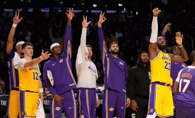 Los Angeles Lakers forward LeBron James, right, shoots as his teammates gesture from the bench during the first half of an NBA basketball game against the Phoenix Suns, Monday, Dec. 1, 2025, in Los Angeles. (AP Photo/Mark J. Terrill)