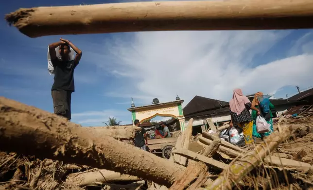 Survivors walk past logs swept away by a flash flood in Batang Toru, North Sumatra, Indonesia, Tuesday, Dec. 2, 2025. (AP Photo/Binsar Bakkara)
