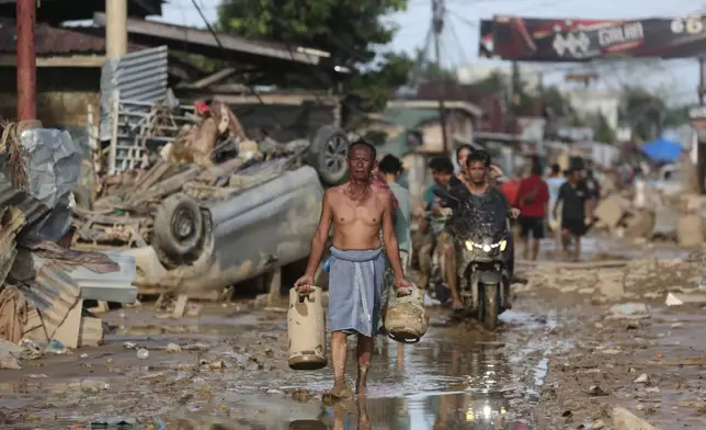 A survivor carries salvaged gas cylinders at an area affected by flash flood in Aceh Tamiang, on Sumatra Island, Indonesia, Thursday, Dec. 4, 2025. (AP Photo/Binsar Bakkara)