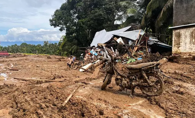 Th wreckage of a motorcycle is seen caked in mud as people inspect the ruin of a house at a village affected by a flash flood in Agam, West Sumatra, Indonesia, Sunday, Nov. 30, 2025. (AP Photo/Ade Yuandha)