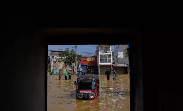 People wade through a submerged area of Colombo, Sri Lanka, following flooding on Sunday, Nov. 30, 2025. (AP Photo/Eranga Jayawardena)