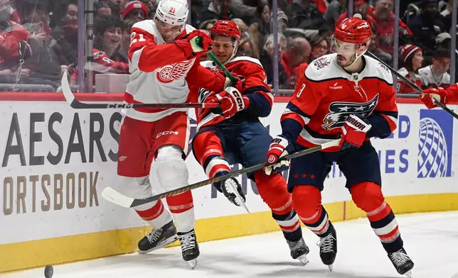 Washington Capitals defenseman Matt Roy, right moves in to gather the puck as Detroit Red Wings left wing James van Riemsdyk, left, knocks Capitals center Nic Dowd to the ice during the second period of an NHL hockey game, Saturday, Dec. 20, 2025, in Washington. (AP Photo/John McDonnell)