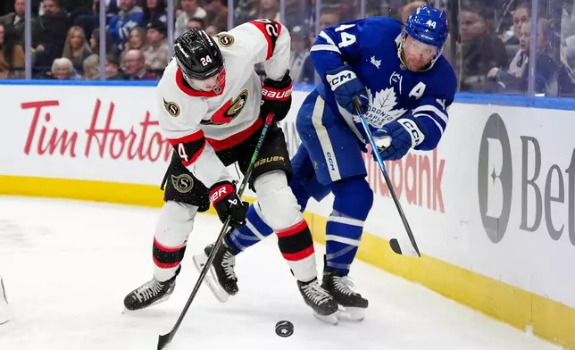 Toronto Maple Leafs defenseman Morgan Rielly, right, and Ottawa Senators center Dylan Cozens vie for control of the puck during the first period of an NHL hockey game in Toronto, Saturday, Dec. 27, 2025. (Frank Gunn/The Canadian Press via AP)