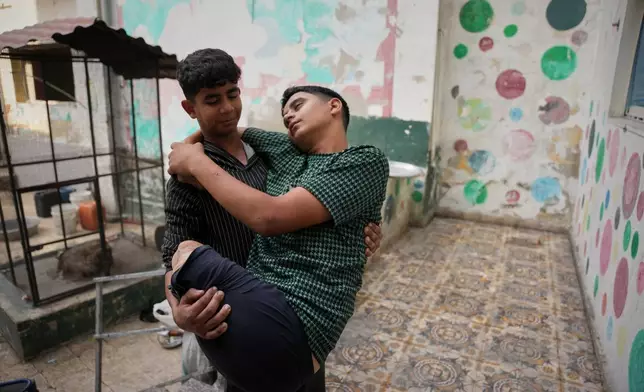 Mohammed Al-Samri, 14, carries his older brother Youssef, 16, who lost his legs while fetching water near their home after an Israeli airstrike in May, in the kindergarten where he was displaced in the Al-Tuffah neighborhood, Gaza City, Monday, Nov. 24, 2025. (AP Photo/Abdel Kareem Hana)