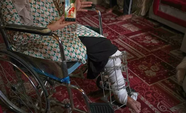 Haneen al-Mabhouh, 34, who lost her leg in an Israeli strike on her home that also killed all four of her daughters, including her 5-month-old baby, shows a photo of one of her daughters on a cellphone while sitting in a wheelchair in her family home in Nuseirat, central Gaza Strip, Thursday, Nov. 6, 2025. (AP Photo/Abdel Kareem Hana)
