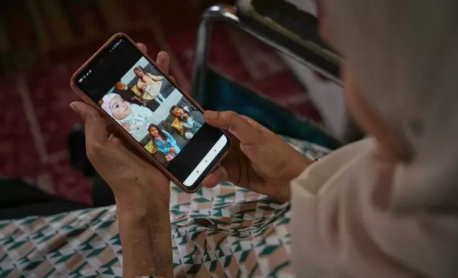 Haneen al-Mabhouh, 34, who lost her leg in an Israeli strike on her home that also killed all four of her daughters, including her 5-month-old baby, looks at photos of her daughters on a cellphone while sitting in a wheelchair in her family home in Nuseirat, central Gaza Strip, Thursday, Nov. 6, 2025. (AP Photo/Abdel Kareem Hana)