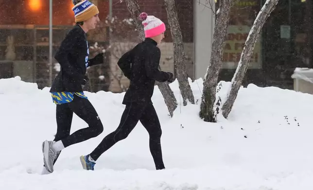Pedestrians run on a snow-covered sidewalk during a snowy day in Wheeling, Ill., Monday, Dec. 1, 2025. (AP Photo/Nam Y. Huh)