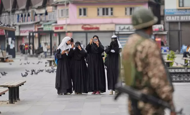 Muslim women take pictures of people marching with the Indian flag, part of a campaign encouraging every household to hoist the national flag, as a paramilitary soldier stands guard, ahead of India's Independence Day in Srinagar, Indian controlled Kashmir, Tuesday, Aug. 12, 2025. (AP Photo/Mukhtar Khan, File)