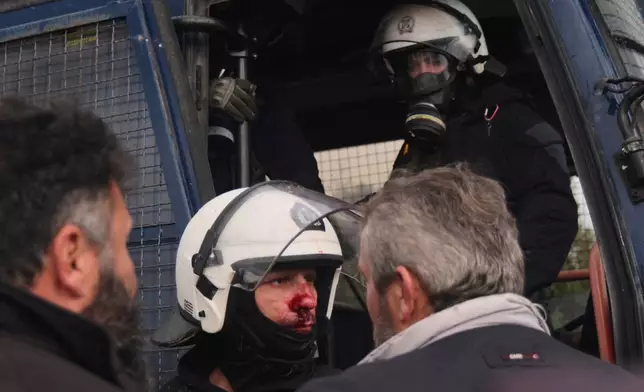 A injured police officer stands next to a police bus during clashes with officers blocking their march to Chania's airport on Crete, Greece, Monday, Dec. 8, 2025, amid protests over delayed EU farm subsidies. (AP Photo/Giannis Angelakis)