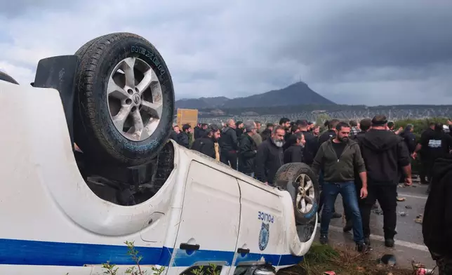 Farmers gather next to an overturned police vehicle during clashes with officers blocking their march to Chania's airport on Crete, Greece, Monday, Dec. 8, 2025, amid protests over delayed EU farm subsidies. (AP Photo/Giannis Angelakis)