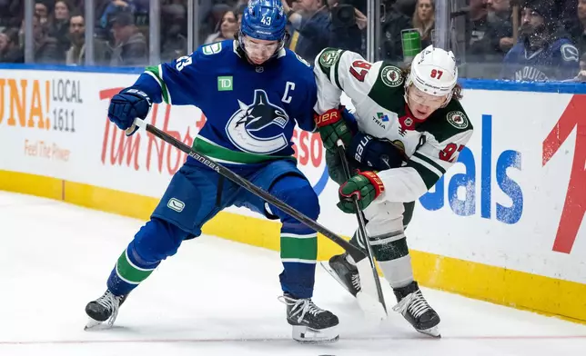Vancouver Canucks Quinn Hughes (43) and Minnesota Wild Kirill Kaprizov (97) vie for the puck during third period NHL hockey game action in Vancouver, British Columbia, Saturday, Dec. 6, 2025. (Ethan Cairns/The Canadian Press via AP)