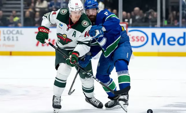 Minnesota Wild Joel Eriksson Ek (14) and Vancouver Canucks Filip Hronek (17) battle for the puck during second period NHL hockey action in Vancouver on Saturday, Dec. 6, 2025. (Ethan Cairns/The Canadian Press via AP)