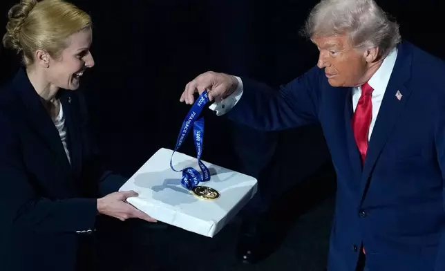 President Donald Trump picks up his FIFA Peace Prize medal, awarded to him by FIFA President Gianni Infantino, before the draw for the 2026 soccer World Cup at the Kennedy Center in Washington, Friday, Dec. 5, 2025. (AP Photo/Julia Demaree Nikhinson)