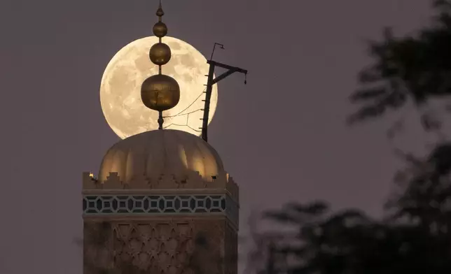A supermoon, the last full moon of the year, rises up behind 12th century Koutoubia mosque in Marrakech, Morocco, Thursday, Dec. 4, 2025. (AP Photo/Mosa'ab Elshamy)
