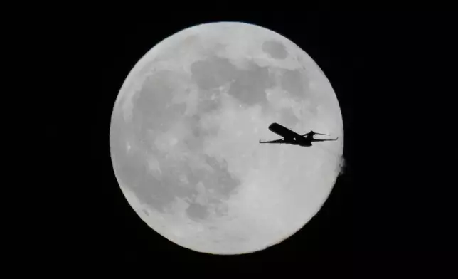 A plane flies past the full moon as the supermoon rises up Thursday, Dec. 4, 2025, in Chicago. (AP Photo/Kiichiro Sato)