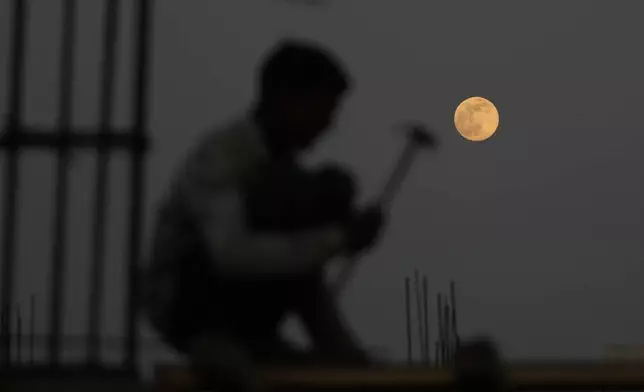 A laborer works at a construction site as a supermoon rises in Ahmedabad, India, Thursday, Dec. 4, 2025. (AP Photo/Ajit Solanki)