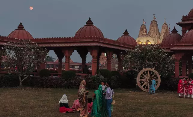 Devotees relax in the garden as a supermoon, the last full moon of the year, rises up on the sky over the Swaminarayan Temple, in Kolkata, India, Thursday, Dec. 4, 2025. (AP Photo/Bikas Das)