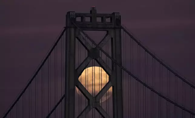 A supermoon, the last full moon of the year, rises behind the San Francisco-Oakland Bay Bridge, Thursday, Dec. 4, 2025, in San Francisco. (AP Photo/Godofredo A. Vásquez)