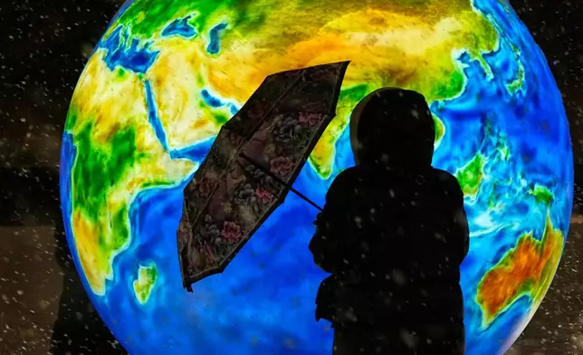 A woman stands next to a glowing ball depicting the Earth at a square decorated prior to Christmas and New Year festivities, during snowfall in St. Petersburg, Russia, Tuesday, Dec. 30, 2025. (AP Photo/Dmitri Lovetsky)