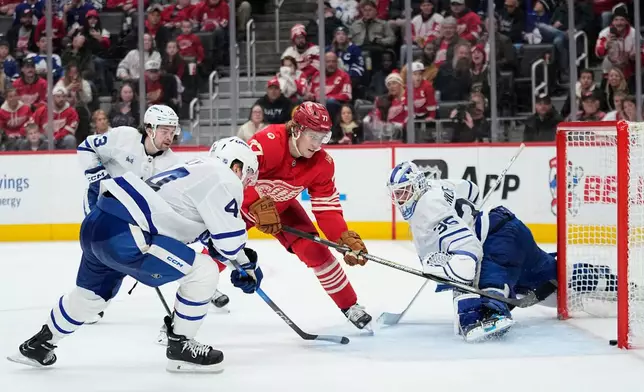 Detroit Red Wings defenseman Simon Edvinsson, third from left, scores the winning goal against Toronto Maple Leafs right wing Easton Cowan, left, defenseman Morgan Rielly, second from left, and goaltender Dennis Hildeby, right, during overtime of an NHL hockey game Sunday, Dec. 28, 2025, in Detroit. (AP Photo/Ryan Sun)