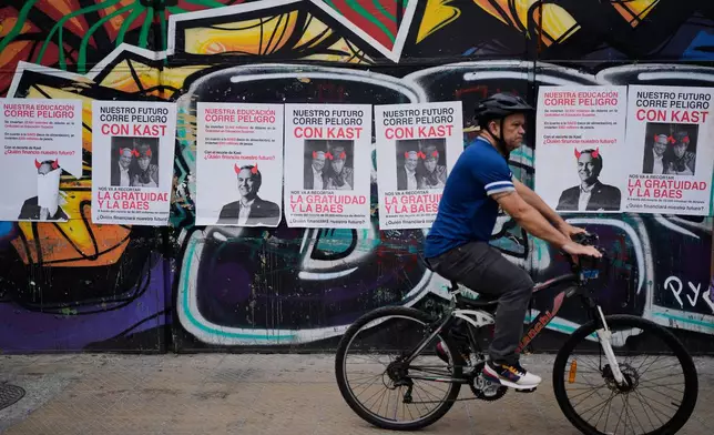 A man cycles past campaign ads for presidential candidate Jose Antonio Kast and Argentina's President Javier Milei reading in Spanish "Our future is in danger" ahead of the presidential runoff election in Santiago, Chile, Friday, Dec. 12, 2025. (AP Photo/Natacha Pisarenko)