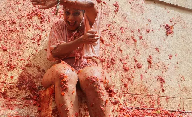 A woman covers herself as revelers throw tomatoes at each other during the annual "Tomatina" tomato fight fiesta, in the village of Bunol near Valencia, Spain, Aug. 27, 2025. (AP Photo/Alberto Saiz, File)