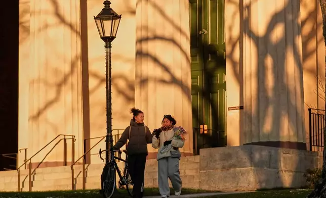 Brown University students Gloria Kuzmenko-Latimir, left, and Haleema Aslam walk by Manning Hall on their way to a makeshift memorial for the shooting victims, Tuesday, Dec. 16, 2025, in Providence, R.I. (AP Photo/Robert F. Bukaty)