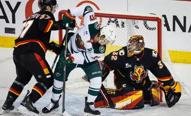 Minnesota Wild's Kirill Kaprizov, centre, is checked by Calgary Flames' Yan Kuznetsov, left, in front of goalie Dustin Wolf, during the first period of an NHL hockey game in Calgary, Alberta, Thursday, Dec. 4, 2025. (Jeff McIntosh/The Canadian Press via AP)
