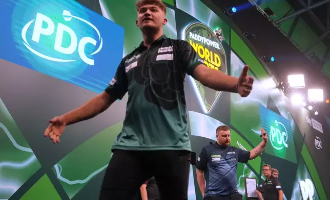 Cameron Menzies of Scotland, rights, reacts after he lost a round one match at the World Darts Championships, at Alexandra Palace in London, Monday, Dec. 15, 2025. (AP Photo/Kin Cheung)