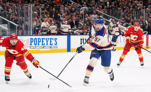 Calgary Flames' Hunter Brzustewicz (48) tries to stop Edmonton Oilers' Connor McDavid (97) from shooting as Flames' Yegor Sharangovich (17) looks on during second period NHL action in Edmonton, Alberta, Tuesday, Dec. 23, 2025. (Amber Bracken/The Canadian Press via AP)