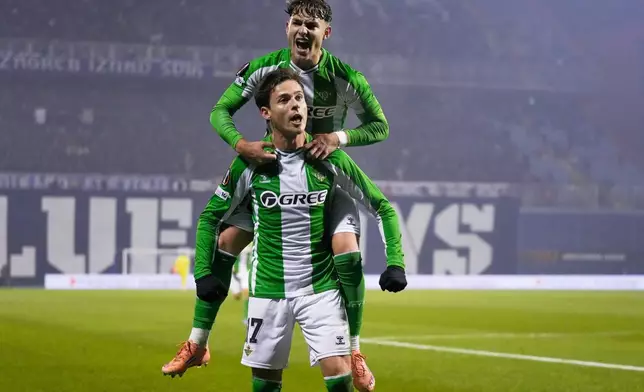 Betis' Rodrigo Riquelme celebrates with Betis' Angel Ortiz, top, after scoring his side's second goal during the Europa League soccer match between GNK Dinamo Zagreb and Real Betis in Zagreb, Croatia, Thursday, Dec. 11, 2025. (AP Photo/Darko Bandic)
