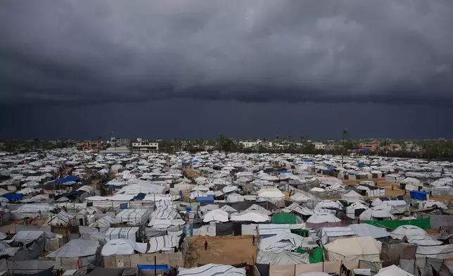 Palestinian children stand on an area surrounded by makeshift tents in a camp for displaced people in Deir al-Balah, central Gaza Strip, Saturday, Dec. 27, 2025. (AP Photo/Abdel Kareem Hana)