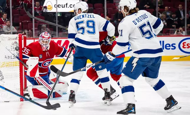 Montreal Canadiens goaltender Sam Montembeault (35) watches the puck go wide of the net as Tampa Bay Lightning' Jake Guentzel (59) and Charle-Edouard D'Astous (51) stand in front during second period NHL hockey action in Montreal on Tuesday, Dec. 9, 2025. (Christopher Katsarov/The Canadian Press via AP)