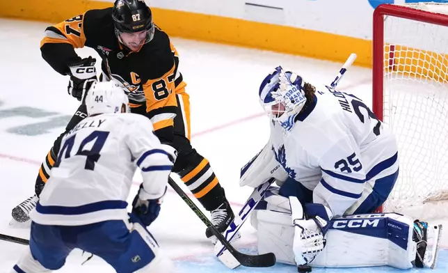 Pittsburgh Penguins' Sidney Crosby (87) backhands a shot past Toronto Maple Leafs goaltender Dennis Hildeby (35) for a goal with Morgan Rielly (44) defending during the third period of an NHL hockey game in Pittsburgh, Saturday, Nov. 29, 2025. (AP Photo/Gene J. Puskar)