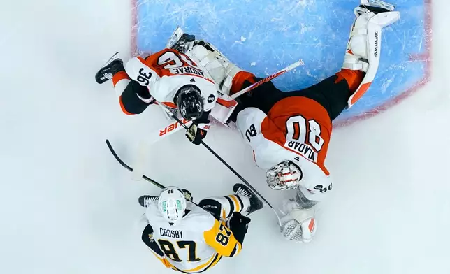 Pittsburgh Penguins' Sidney Crosby (87) scores a goal against Philadelphia Flyers' Dan Vladar (80) and Emil Andrae (36) during the first period of an NHL hockey game Monday, Dec. 1, 2025, in Philadelphia. (AP Photo/Matt Slocum)