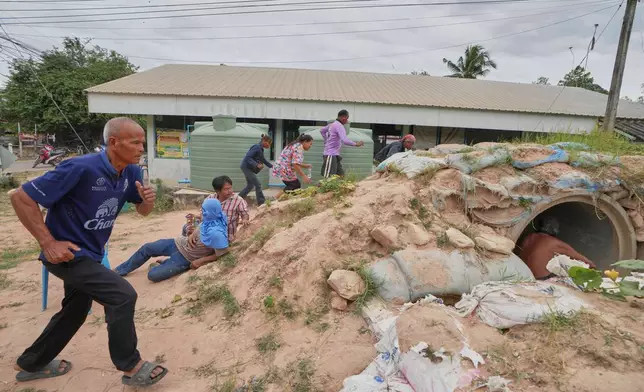Village security volunteers and resident run into shelter while the blasts sounded too close in Buriram province, Thailand, Friday, Dec. 12, 2025, following renewed border conflict between Thailand and Cambodia. (AP Photo/Sakchai Lalit)