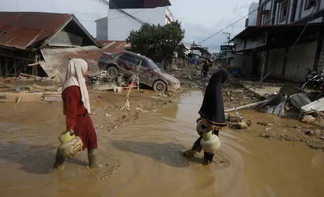 FILE - Survivors walk past the wreckage of a car at an area affected by flash flooding in the aftermath of Cyclone Senyar in Aceh Tamiang, on Sumatra Island, Indonesia, Thursday, Dec. 4, 2025. (AP Photo/Binsar Bakkara, File)