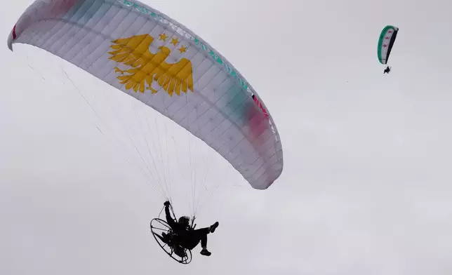 Powered paragliders fly over a gathering during celebrations marking the first anniversary of the ousting of former President Bashar Assad, with Mount Qasioun seen in the background, in Damascus, Syria, Monday, Dec. 8, 2025. (AP Photo/Hussein Malla)