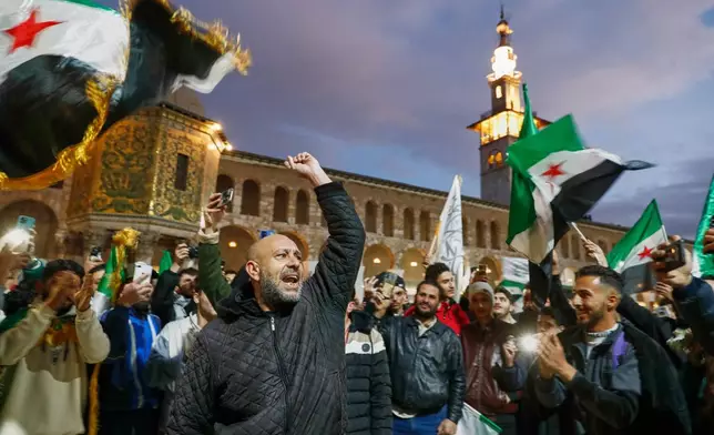 Syrians shout slogans and wave flags outside the Umayyad Mosque before a prayer held ahead of celebrations marking the first anniversary of the ousting of the Bashar Assad regime in Damascus, Syria, Monday, Dec. 8, 2025. (AP Photo/Omar Sanadiki)